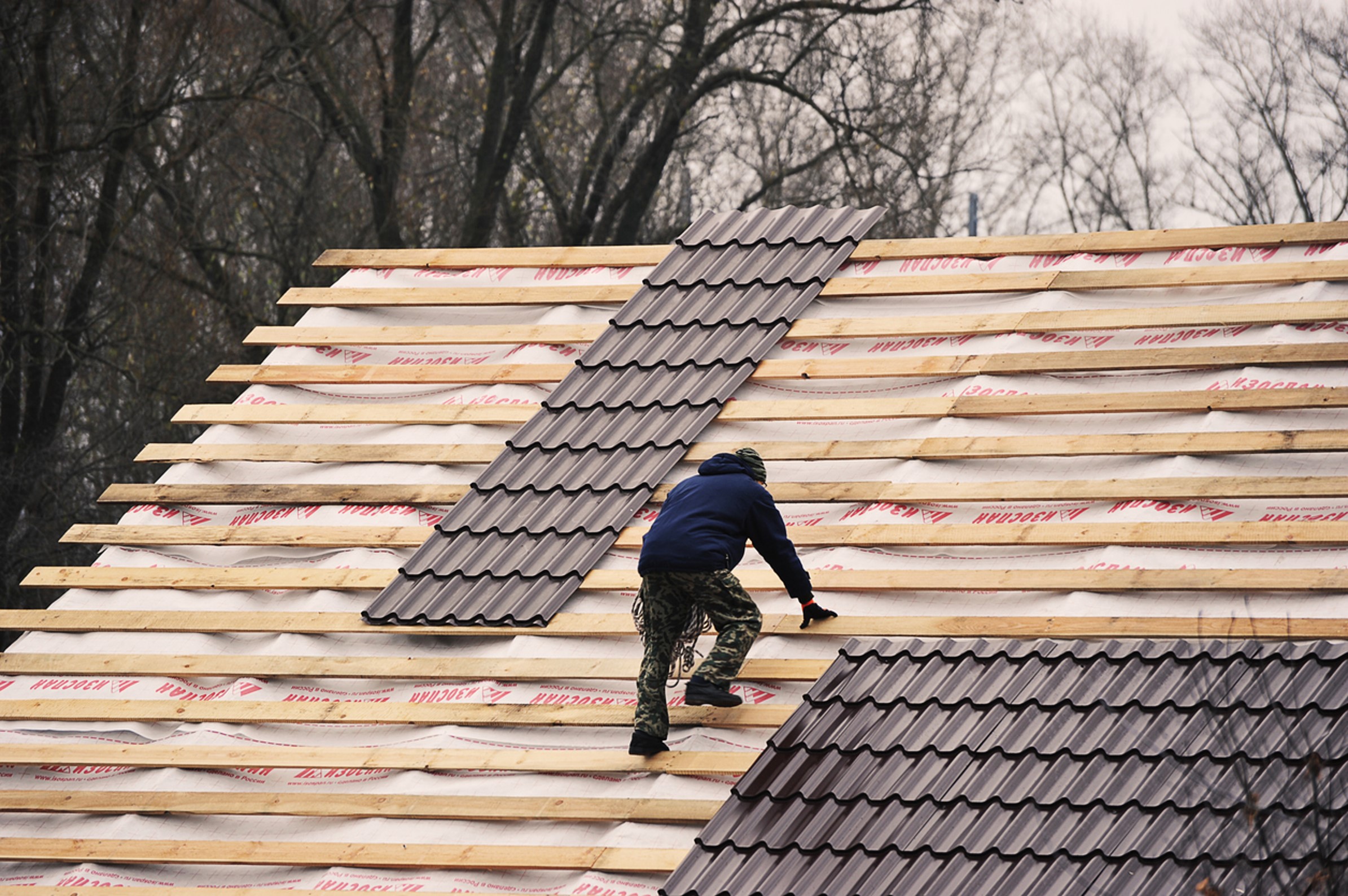 A Man Wearing Cup and Blue Coat Working on a Roof